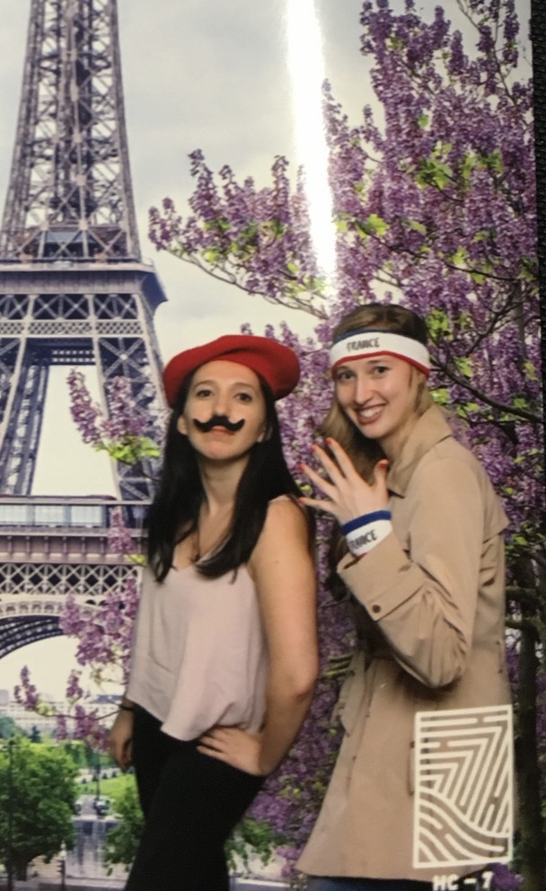 Two teammates posing with playful props at a Paris-themed photo booth